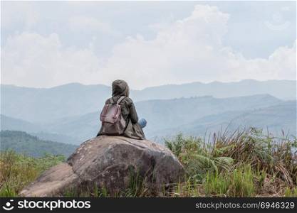 Hipster girl sitting in rocky of mountain . Hipster girl with backpack sitting in a rocky top of the mountain against the blue of sky