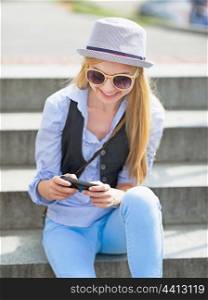 Hipster girl writing sms while sitting on stairs