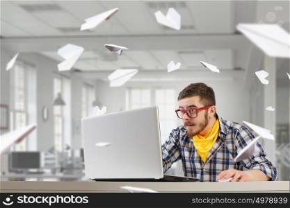 Hipster guy use laptop. Young emotional guy in red glasses surfing the Internet