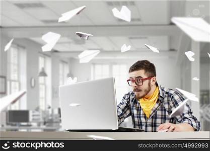 Hipster guy use laptop. Young emotional guy in red glasses surfing the Internet