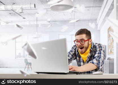 Hipster guy use laptop. Young emotional guy in red glasses surfing the Internet