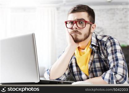 Hipster guy use laptop. Young pensive guy in red glasses surfing the Internet