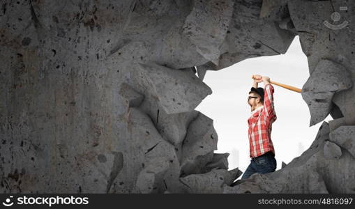 Hipster guy with bat. Furious hipster guy breaking wall with baseball bat