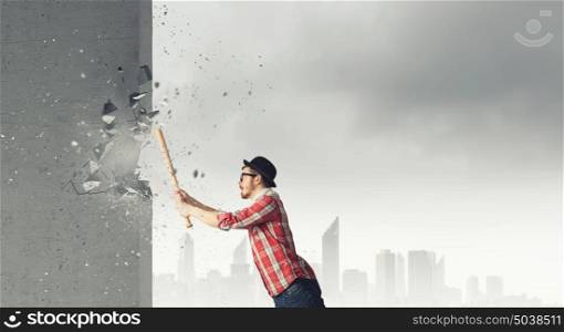 Hipster guy with bat. Furious hipster guy breaking wall with baseball bat