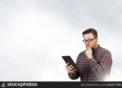 Hipster guy with tablet device. Young thoughtful man in checked shirt using tablet pc