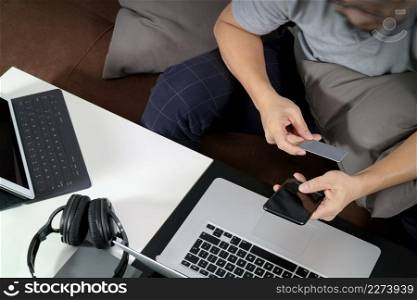 hipster hand using smart phone and laptop compter,digital tablet docking keyboard,holding cradit card payments online business,sitting on sofa in living room,work at home concept