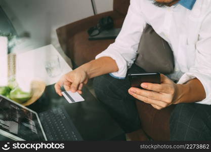 hipster hand using smart phone and laptop compter,holding cradit card payments online business,sitting on sofa in living room,green apples in wooden tray,filter