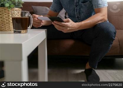 hipster hand using smart phone,digital tablet docking keyboard,holding cradit card payments online business,sitting on sofa in living room,work at home concept