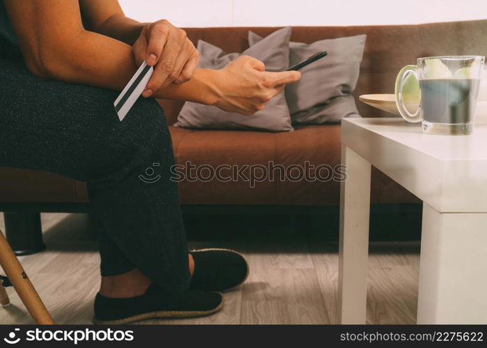 hipster hand using smart phone,digital tablet docking keyboard,holding cradit card payments online business,sitting on sofa in living room,work at home concept,filter effect