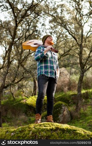Hipster man with red beard and a guitar relaxs in the field