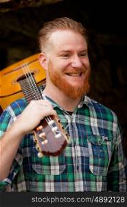 Hipster man with red beard holding a guitar in a rustic house