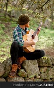 Hipster man with red beard playing a guitar in the field