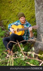Hipster man with red beard playing a guitar in the field