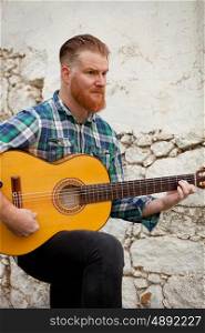 Hipster man with red beard playing a guitar with a old wall of background