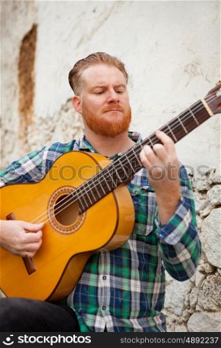 Hipster man with red beard playing a guitar with a old wall of background