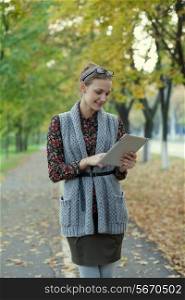 Hipster style young woman using tablet pc in autumn street
