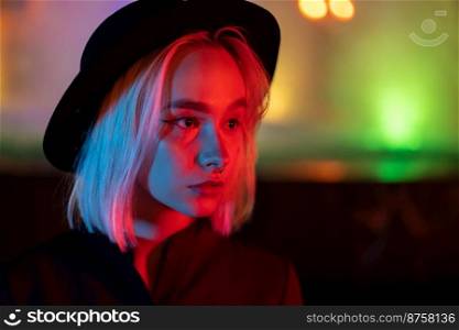 Hipster woman with blond hairstyle standing on neon glowing background. City at night. Hat, nose piercing. Beautiful attractive girl. High quality photo. Hipster woman with blond hairstyle standing on neon glowing background. City at night. Hat, nose piercing. Beautiful attractive girl.