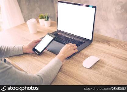 Hipster women holding phone and using laptop on wooden table in coffee shop.
