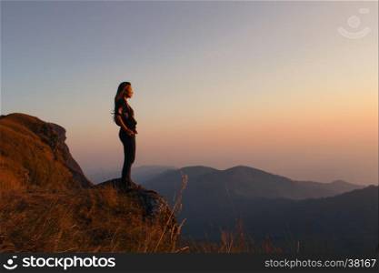 Hipster young girl with backpack enjoying sunset on peak of foggy mountain. Tourist traveler on background view mockup. Hiker looking sunlight in trip in Thailand country. Vintage filtered image.