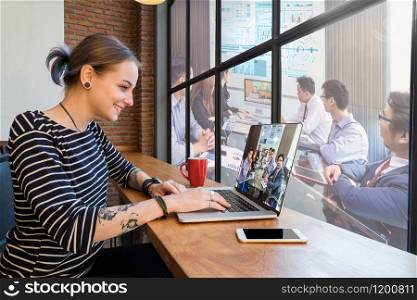 Hipster young Woman freelancer using the technology laptop having video conference via monitor display for working in the Loft cafe workplace. Creative Startup and entrepreneur business concept