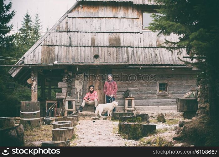 hipsters couple portrait, two young man with white husky dog sitting in front of old wooden retro house
