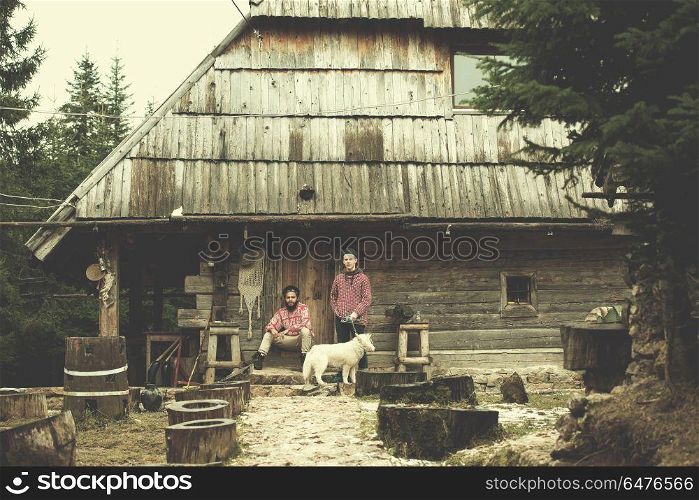 hipsters couple portrait, two young man with white husky dog sitting in front of old wooden retro house. frineds together in front of old wooden house