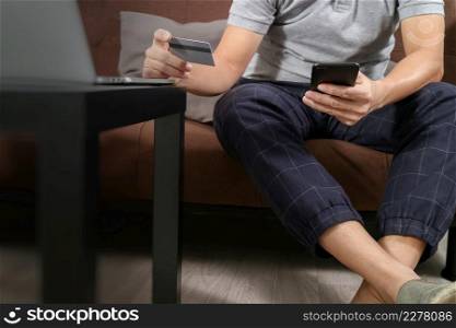 hipsterusing smart phone and laptop computer and holding credit card for payments online business,sitting on sofa in living room,work at home concept