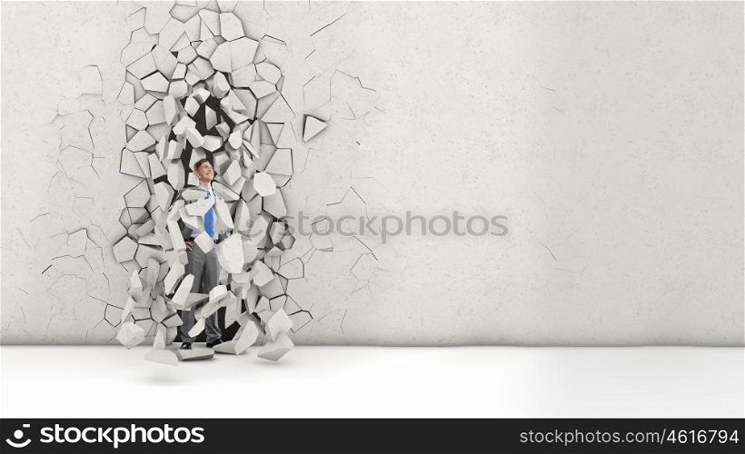 His breakthrough in business. Young powerful businessman breaking through cement wall