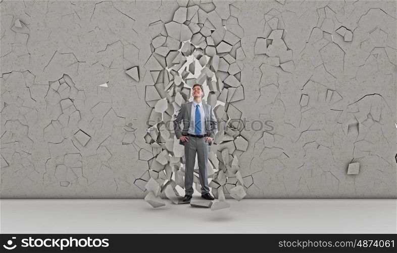 His breakthrough in business. Young powerful businessman breaking through cement wall