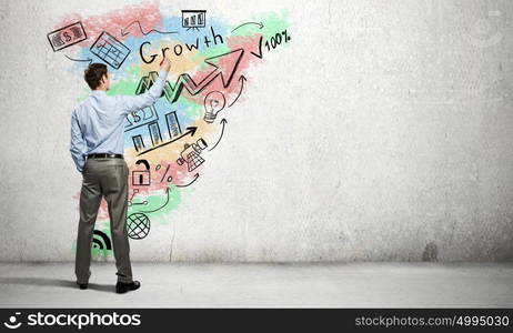 His bright strategy plan . Back view of businessman drawing business sketches on wall