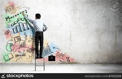 His bright strategy plan . Back view of businessman standing on ladder and drawing ideas on wall