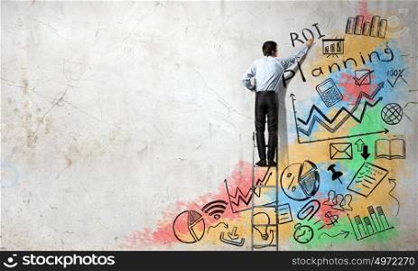 His bright strategy plan . Back view of businessman standing on ladder and drawing ideas on wall