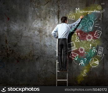 His bright strategy plan . Back view of businessman standing on ladder and drawing ideas on wall