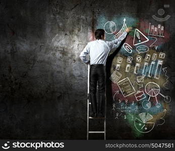 His bright strategy plan . Back view of businessman standing on ladder and drawing on wall