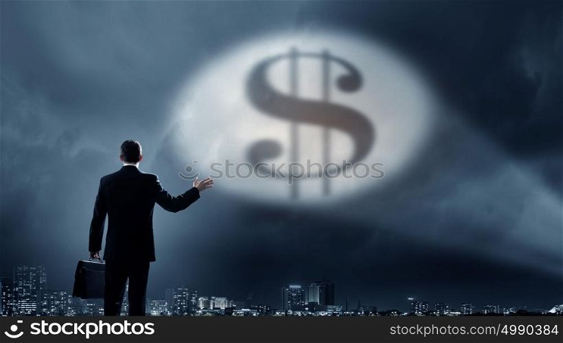 His goal is to become rich. Businessman standing with back in darkness and dollar sign in spothlight