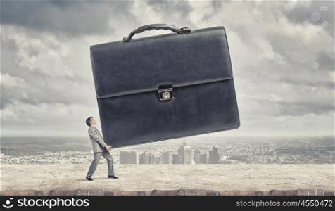 His job is not easy for him. Young determined businessman carrying big heavy suitcase