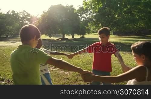 Hispanic and african american little boys and girls playing ring around the rosie in city park and holding hands. Young kids, friends, people, recreation, summer camp fun