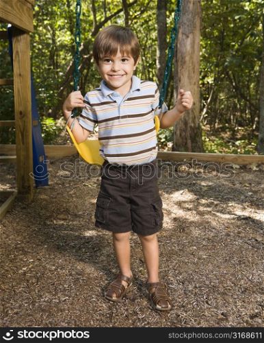 Hispanic boy standing by swing set smiling at viewer.