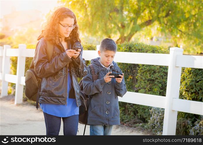Hispanic Brother and Sister Wearing Backpacks Walking Texting On Cell Pones.