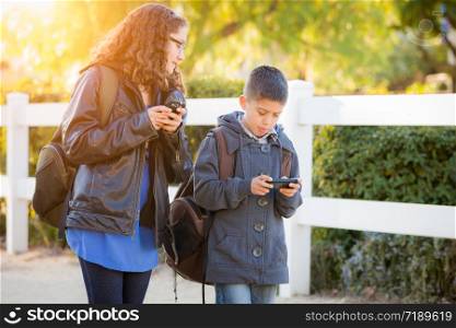 Hispanic Brother and Sister Wearing Backpacks Walking Texting On Cell Pones.