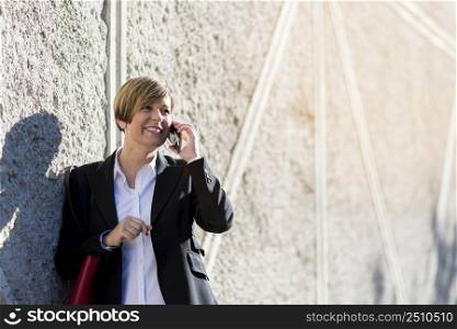 Hispanic businesswoman smiling speaks on a mobile outside