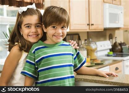 Hispanic children in kitchen smiling at viewer.