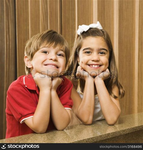 Hispanic children with their head on hands smiling at viewer.
