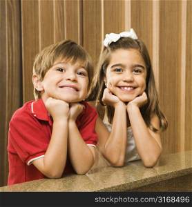Hispanic children with their head on hands smiling at viewer.