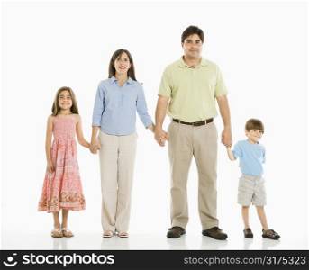 Hispanic family of four standing against white background holding hands.