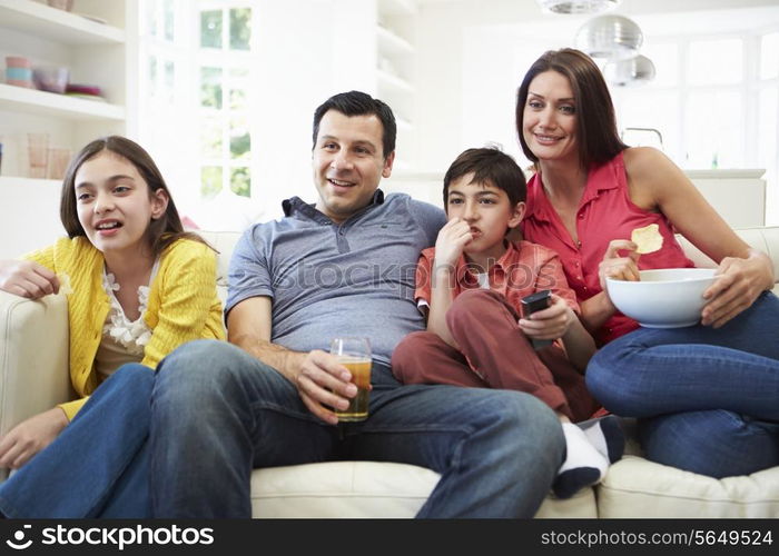 Hispanic Family Sitting On Sofa Watching TV Together