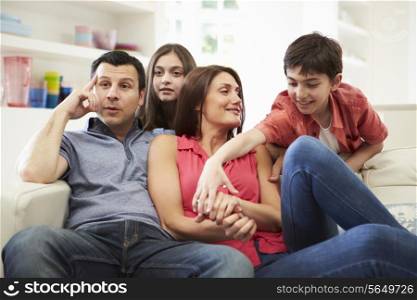 Hispanic Family Sitting On Sofa Watching TV Together