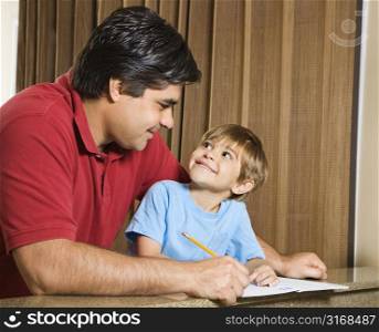 Hispanic father and son doing homework and making eye contact.