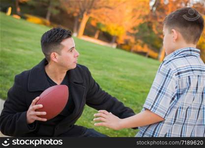 Hispanic Father Holding Football Teaching Young Boy.