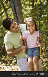 Hispanic father pushing daughter on swing.